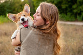 Portrait: young woman with laughing corgi puppy, nature background