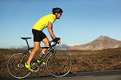 Biking cyclist male athlete going uphill on open road training hard on bicycle outdoors at sunset. Nature landscape.