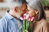 Elderly couple in love hugging on Valentine's day. A loving   husband gives his wife a  bouquet of tulip