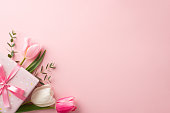 Mother's Day concept. Top view photo of stylish pink giftbox with ribbon bow and bouquet of tulips on isolated pastel pink background with copyspace