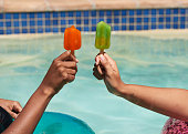 Close up of friends holding ice lolly popsicles in the swimming pool, beat heat