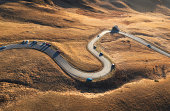 Aerial view of winding road in mountain pass at sunset in golden autumn. Passo Giau, Dolomites, Italy. Beautiful curving roadway, cars, orange grass, alpine meadows. Landscape with highway in fall