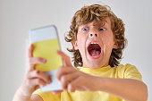 Yelling boy taking selfie on smartphone on light background