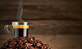 Cup glass of coffee with smoke and coffee beans on old wooden background