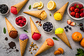 Multicolored ice cream cones and fruits shot from above on gray background