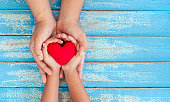 Red heart in child kid and mother hands on old blue wooden table