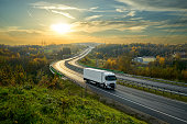 White truck driving on the highway winding through forested landscape in autumn colors at sunset